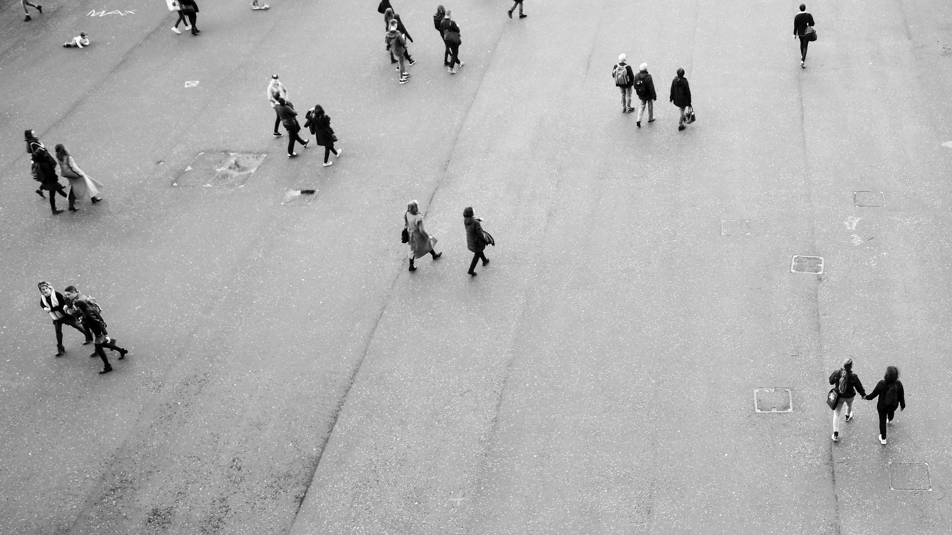People walking across a wide city plaza, seen from above in black and white
